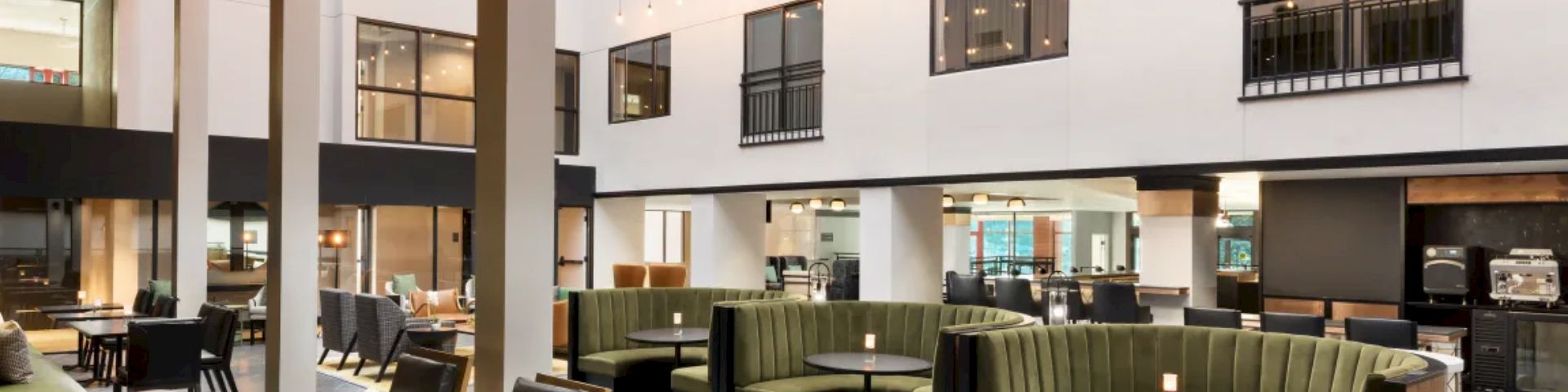 A modern hotel lobby with a foosball table, comfy green couches, and open seating, bright natural light, white walls, and stylish decor.