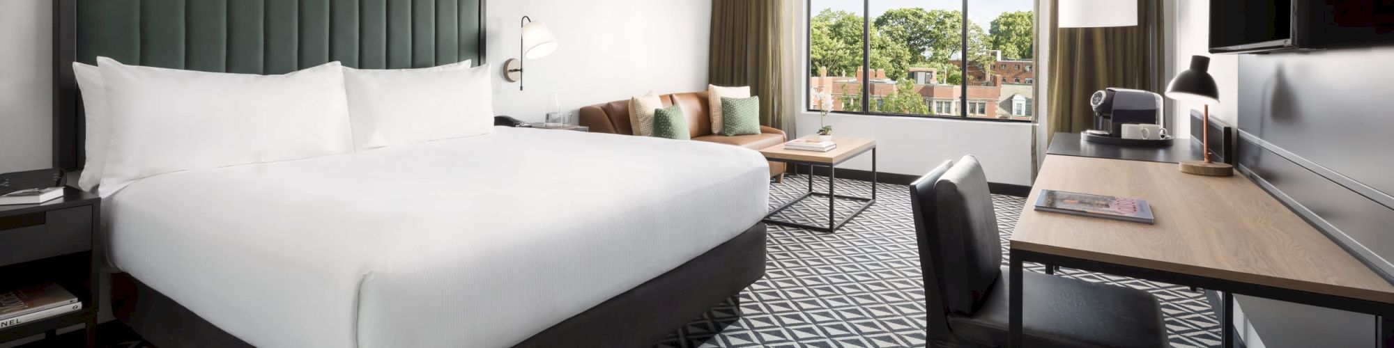 A modern hotel room with a large bed, patterned carpet, desk, chair, and a view of trees through a window. Update complete.