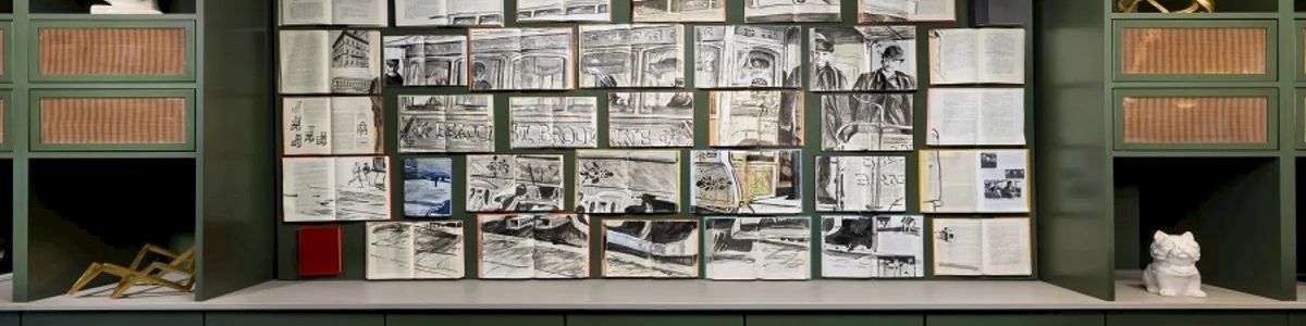 A wall of green cabinets with a central bulletin board filled with black-and-white newspaper clippings and photos, plus decorative shelves and white figurines.