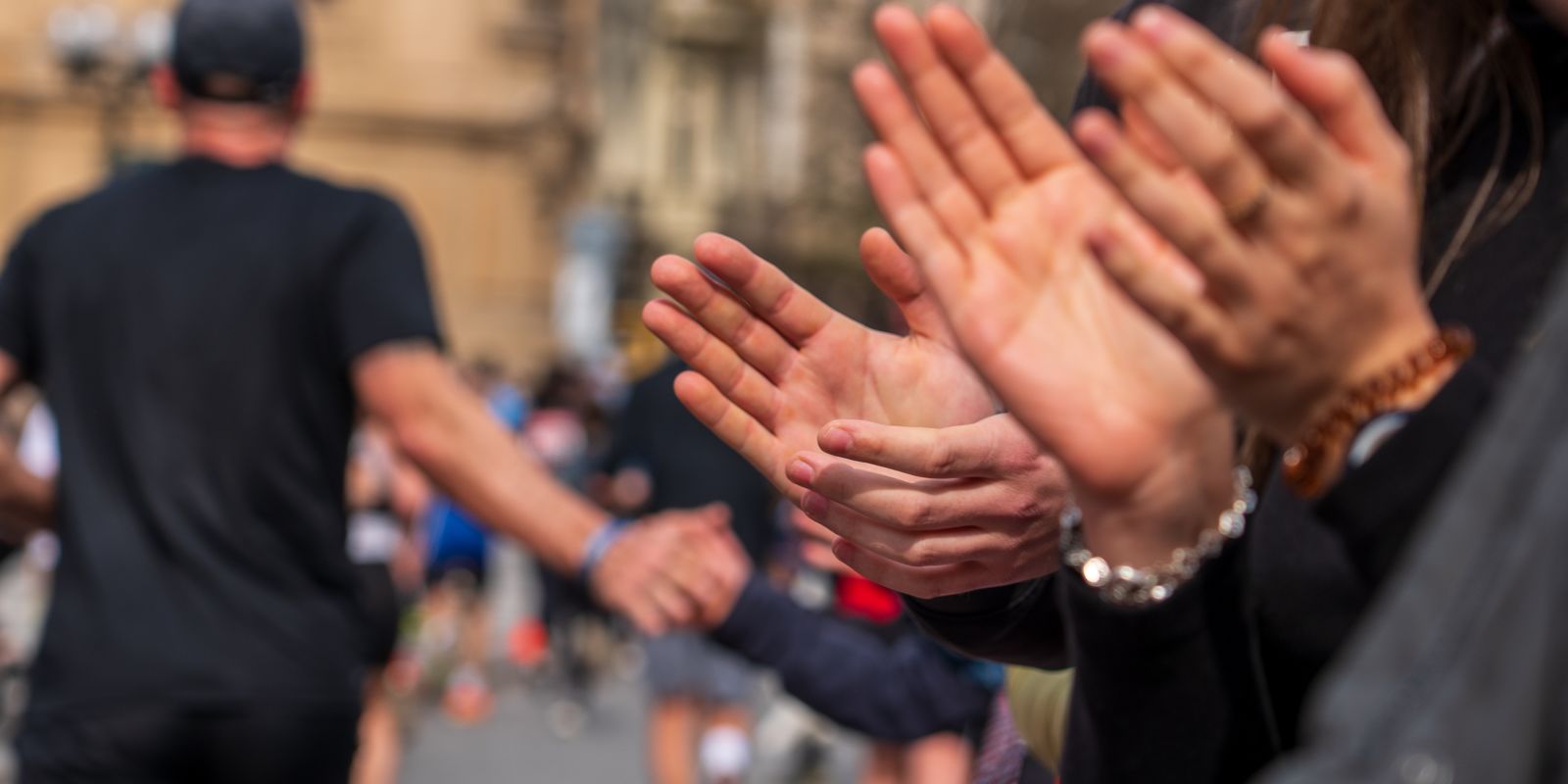 A line of people claps along a street, cheering as runners pass by, capturing a moment of support and celebration.
