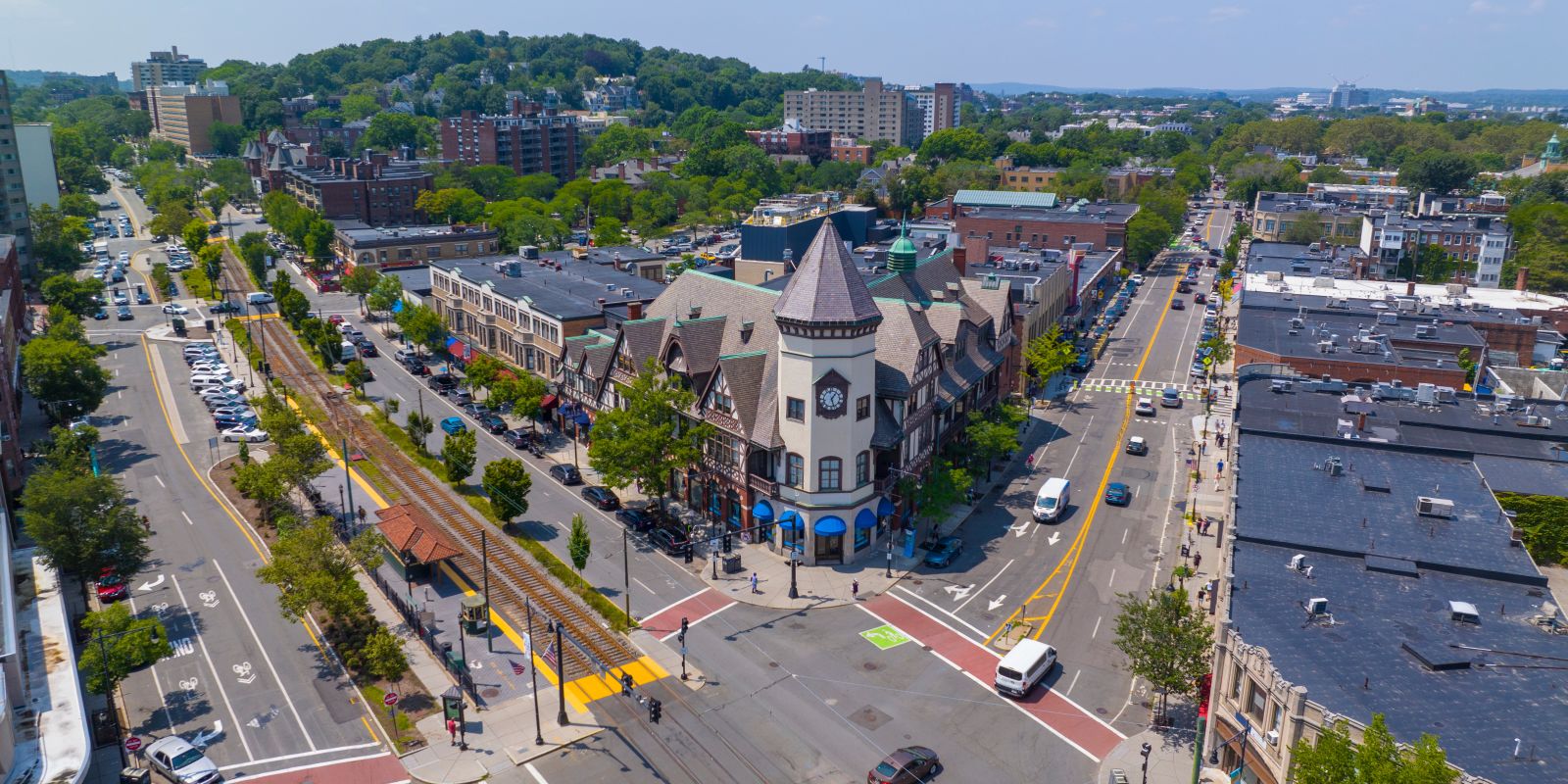 Aerial view of a small city center with a central clock tower building, streets, cars, and trees surrounding a busy intersection.