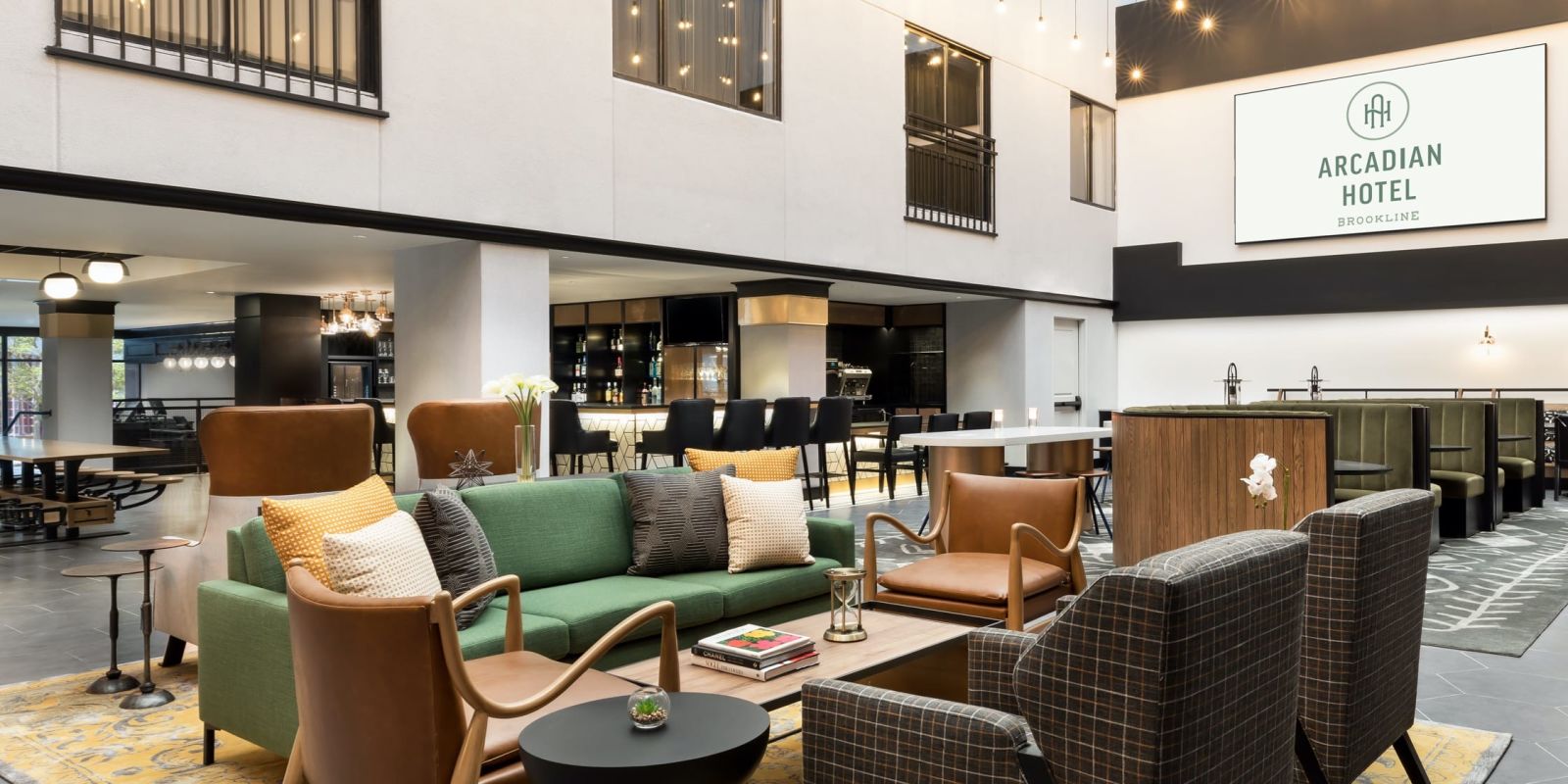 Hotel lobby lounge area with colorful sofas, modern chairs, coffee tables, and a reception desk; Arcadian Hotel signage visible. (approx 134 chars)
